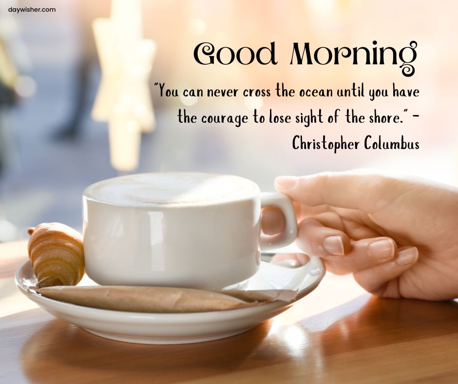 A motivational morning image featuring a steaming cup of coffee and a croissant on a saucer held by a hand, next to a quote by Christopher Columbus, "You can never cross the ocean until