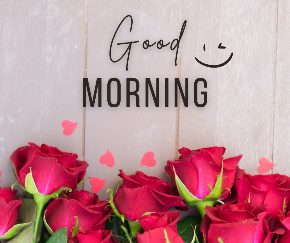 A vibrant arrangement of red roses against a rustic wooden background, accompanied by playful pink heart confetti and a whimsical "Good Morning" greeting with a smiling face. This image combines the freshness of red roses with a touch of cheerful graphics, making it a delightful morning greeting to brighten anyone's day.
