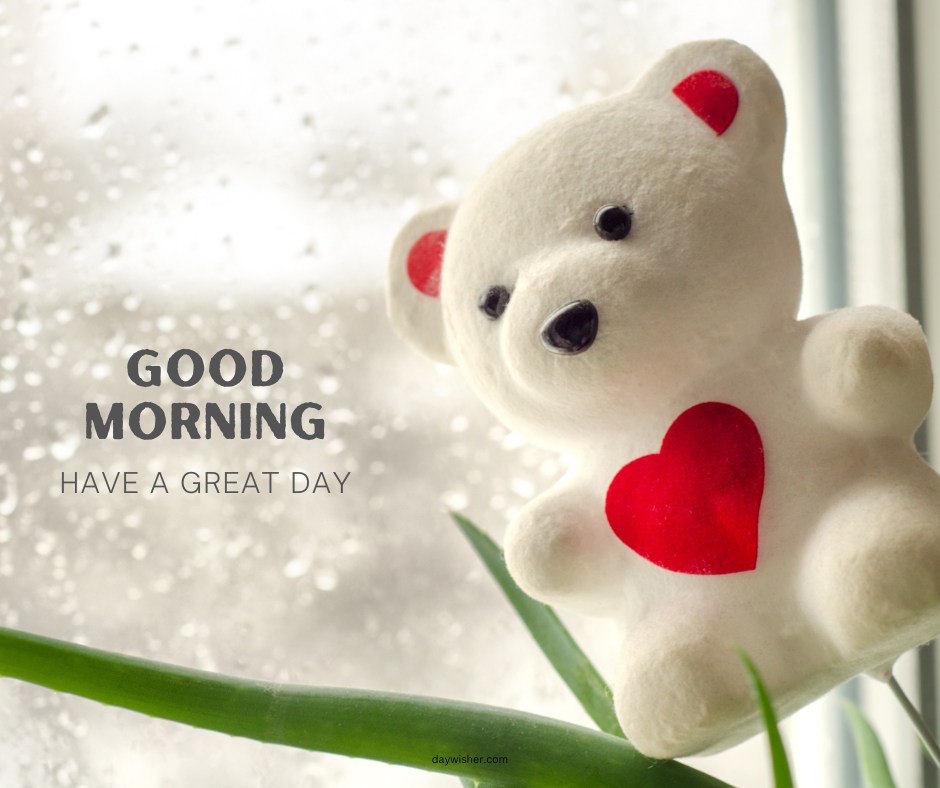 A white good morning teddy bear with a red heart, sitting by a window on a rainy day. The image features the text "Good Morning - Have a Great Day," creating a cozy and uplifting scene.