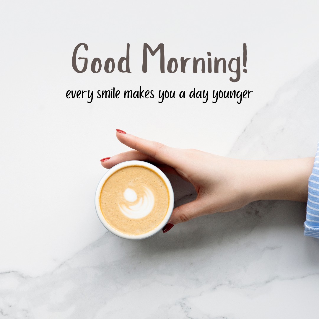 A woman's hand delicately holding a cup of coffee featuring beautiful latte art on a white marble background, accompanied by the inspirational message "Good Morning! Every smile makes you a day younger," ideal for those who love good morning coffee images that blend inspiration with elegance.